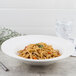 A Villeroy & Boch white porcelain pasta plate with a bowl of noodles and a sprig of rosemary on a white background.