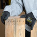 A person wearing Cordova Monarch black engineered fiber cut resistant gloves with black latex palm coating holding a piece of wood.