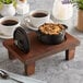 A Valor 8 oz. Pre-Seasoned Mini Cast Iron Pot with Cover on a wooden stand with cups of coffee and a plant.