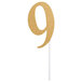 A gold number 9 cake topper on a white stick.