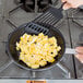 A person cooking scrambled eggs in a Vollrath non-stick fry pan.
