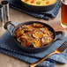 A Valor pre-seasoned cast iron round casserole dish filled with food with a fork on a napkin next to a glass of beer.