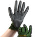 A hand wearing Cordova Monarch cut resistant gloves with a black polyurethane palm coating and green engineered fiber.