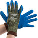 A pair of medium Cordova blue and green cut resistant gloves with blue latex palms being worn by a pair of hands.
