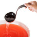 A hand holding a Fineline black plastic ladle pouring red liquid into a bowl.