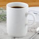 A close-up of a white Villeroy & Boch coffee cup with a handle on a table with a spoon.