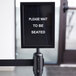 A Lancaster Table & Seating Stanchion sign with clear covers on a pole. The sign is black with white text.