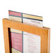 A Menu Solutions Country Oak wood frame holding a menu on a wooden table.