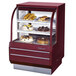 A red Turbo Air curved glass refrigerated bakery display case filled with cakes and pastries on shelves.