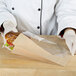 A person in gloves holding a Bagcraft Packaging Dubl View ToGo! Kraft large window sandwich bag with a sandwich inside.
