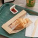 A croissant in a Bagcraft Kraft window paper bag on a green tray.