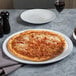 An American Metalcraft white ceramic pizza serving tray with a pizza on it on a table in an Italian restaurant.
