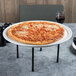 A pizza on an American Metalcraft white ceramic pizza serving tray on a table with wine glasses.