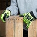 A person wearing lime green and yellow Cordova OGRE work gloves holding a piece of wood.