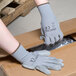 A person wearing Cordova gray polyester gloves with gray polyurethane palm coating opening a box.