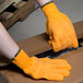 A person wearing Cordova orange warehouse gloves opening a box.