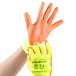 A hand wearing a Cordova yellow and orange warehouse glove with orange palm coating.