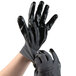 A person putting on a pair of gray Cordova warehouse gloves with black nitrile palm coating.
