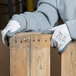 A person wearing Cordova white nylon gloves with gray nitrile palm coating holding a piece of wood.