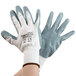 A person wearing Cordova white nylon gloves with gray foam nitrile coating on the palms.