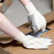 A person wearing Cordova medium weight cotton canvas gloves with black PVC dots on the palm is putting a box on a table.