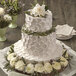 A white wedding cake with flowers on top displayed on a table with a Wilton floral cake spike.