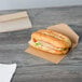 A sandwich in a Bagcraft Packaging paper bag with a window on a table.