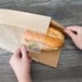 A person's hand holding a Bagcraft Kraft paper bag with a sandwich inside.
