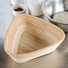 A Matfer Bourgeat triangle-shaped willow bread basket with a bowl of dough inside.