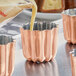 A Matfer Bourgeat copper cannele mold being filled with liquid.