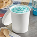 A white paper food cup filled with blue ice cream with a wooden spoon.