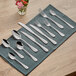 A group of Acopa stainless steel table knives on a blue cloth with a napkin.
