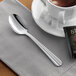 An Acopa Harmony stainless steel teaspoon on a table next to a cup of tea.