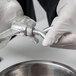 A person in white gloves using the Weston Corn and Grain Grinder to hold a metal piece over a silver bowl.