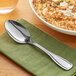 An Acopa Saxton stainless steel oval bowl spoon on a napkin next to a bowl of rice.