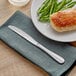 An Acopa Benson stainless steel dinner knife on a plate with chicken and green beans.