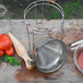 A metal strainer and pestle set next to tomatoes.