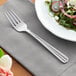 An Acopa Harmony stainless steel salad fork on a napkin next to a plate of salad.