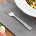 An Acopa Harmony stainless steel dinner fork on a napkin next to a plate of pasta.