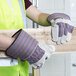 A person wearing Cordova striped canvas work gloves with leather palm coating and rubber cuffs holding a piece of wood.