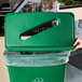 A hand attaching a green Lavex Slim Rectangular Recycling trash can lid to a green trash can.