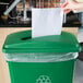 A hand putting white paper into a green Lavex Slim Recycling bin.