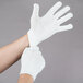 A person wearing Cordova white polyester work gloves.