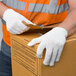 A person wearing Cordova medium weight white polyester work gloves and holding a box.