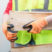 A person wearing Cordova Hi-Vis orange warehouse gloves with black foam nitrile palm coating holding a piece of wood.