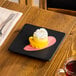 A 6-inch square matte black stoneware flat plate with a dessert served on it.