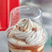 A clear plastic dome lid on a cup of ice cream with whipped cream.
