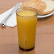 A light amber Cambro plastic tumbler filled with orange juice on a table next to a bagel.
