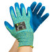A pair of medium Cordova blue and yellow cut resistant gloves with blue crinkle latex palms on a pair of hands.
