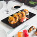 A rectangular matte black stoneware plate with sushi on it on a table.